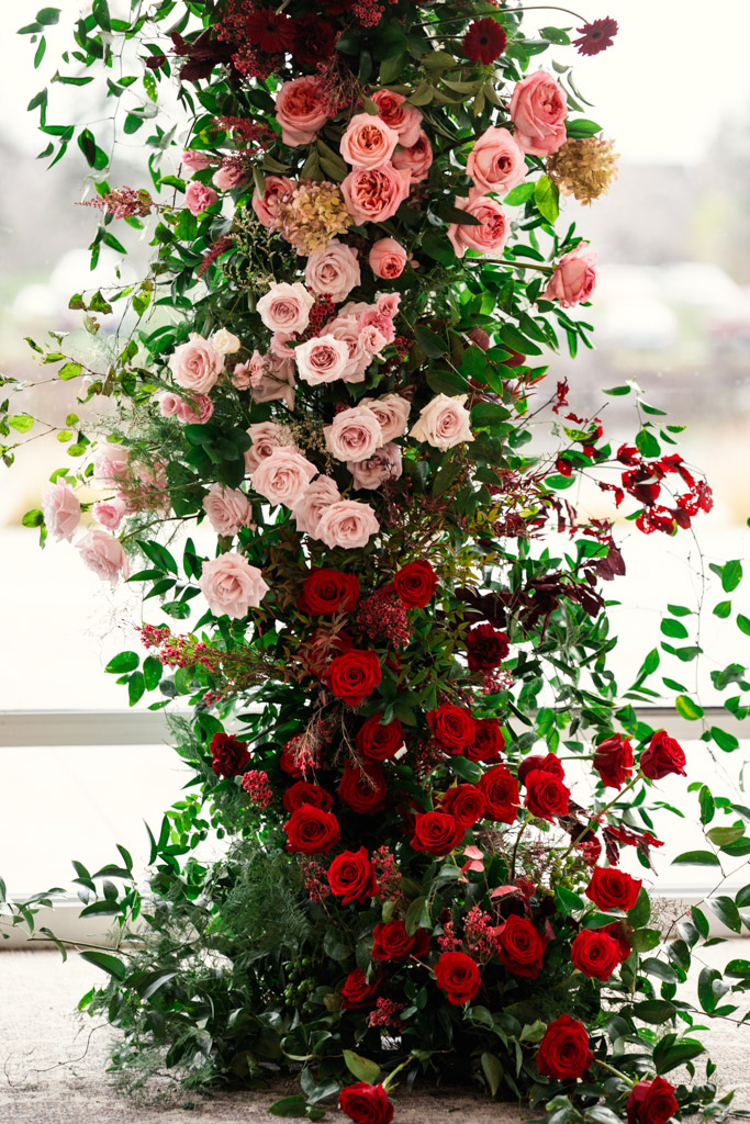 A tall floral arrangement with red and pink roses and greenery is beautifully displayed against in wedding ceremony space at Lincolnshire Marriott Resort