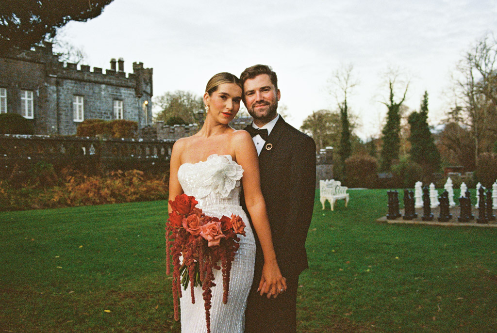 Portrait of bride and groom standing together outdoors, holding hands, with Markree Castle and its lush garden in the background