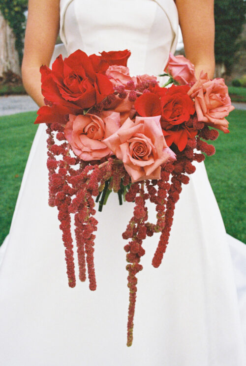 Bride in white dress holding bouquet of red and pink roses with cascading red hanging flowers at a romantic Markree Castle wedding.