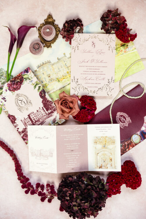 Flat lay of elegant Markree Castle wedding invitations, flowers, pearls, and vintage decor on a blush pink background.