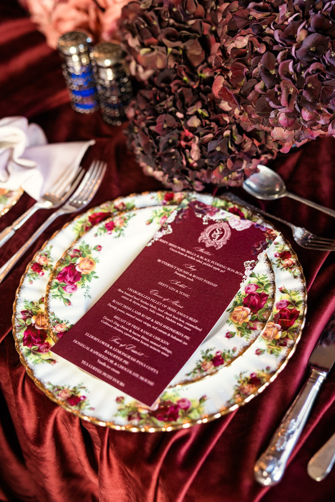Floral china plates with a burgundy menu card, silverware, napkin, and dried hydrangea centerpiece for a Markree Castle wedding reception