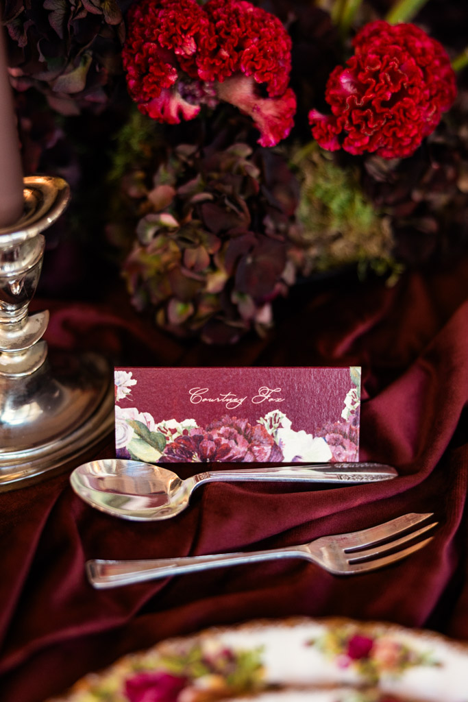 Guest place card on a burgundy tablecloth with red flowers, silverware, and a candlestick for Markree Castle wedding reception