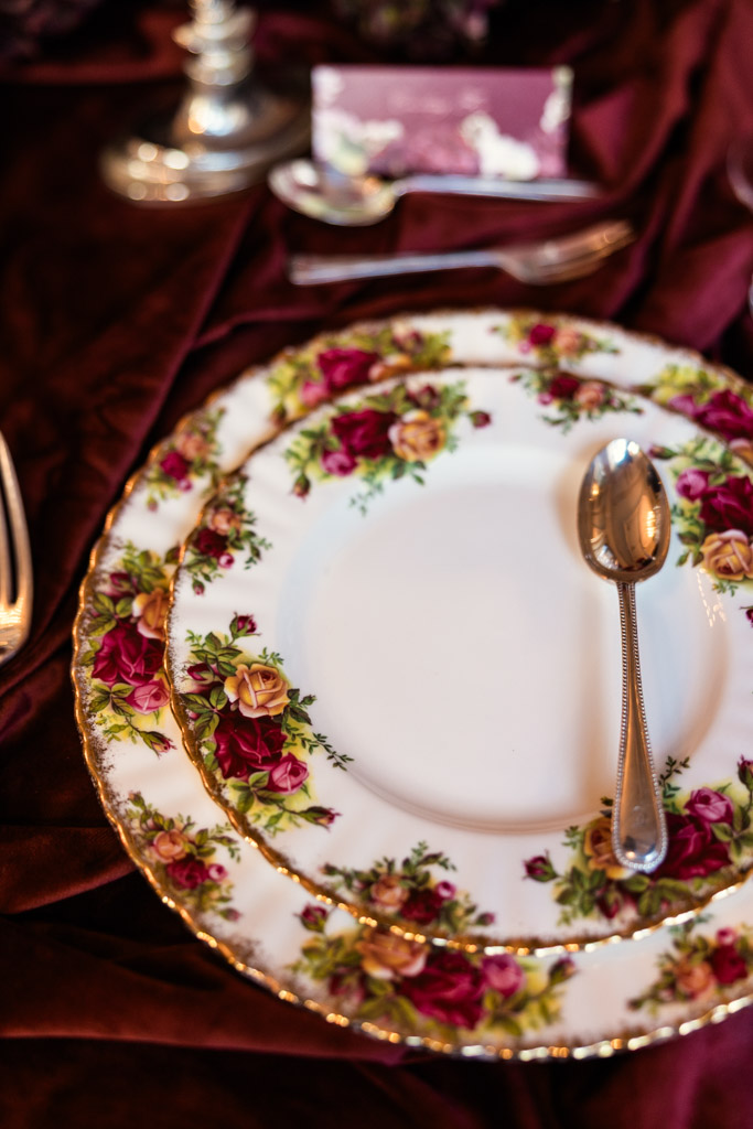 Floral china plates with a silver spoon on a burgundy tablecloth in a guest place setting for Markree Castle wedding reception