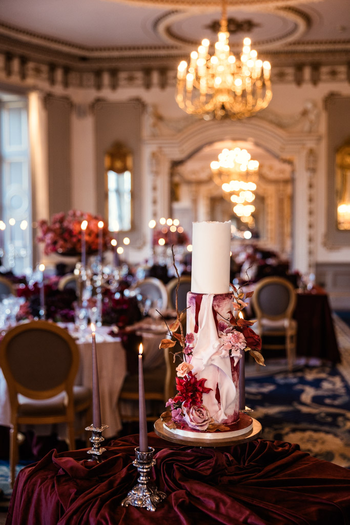 A tall, elegant cake with floral decorations stands in a lavish, chandelier-lit banquet hall, inside Markree Castle