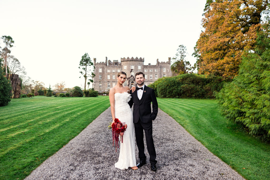 Bride and groom pose on a path outside Markree Castle, surrounded by green lawns and trees