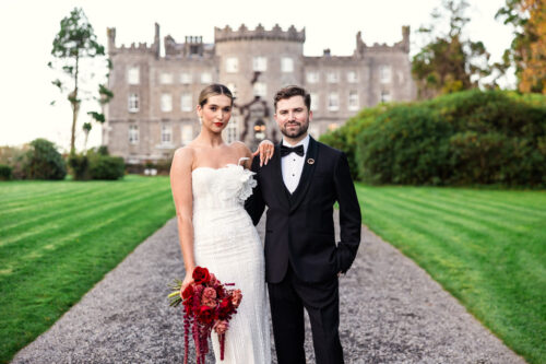 A bride and groom pose on a garden path in front of Markree Castle, both dressed formally for their enchanting Markree Castle wedding.