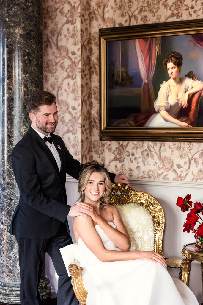 Photo of groom in a tuxedo standing beside bride in a white dress sitting on an ornate gold chair at Markree Castle