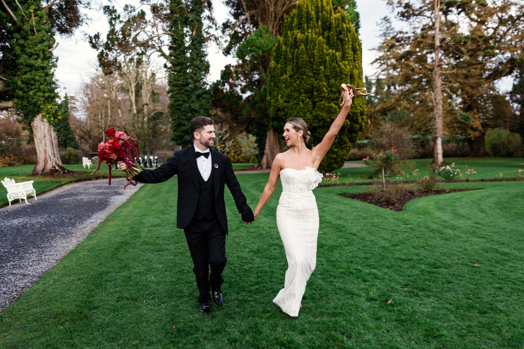 Bride and groom holding hands, walking on grass, smiling and celebrating in a garden outside Markree Castle