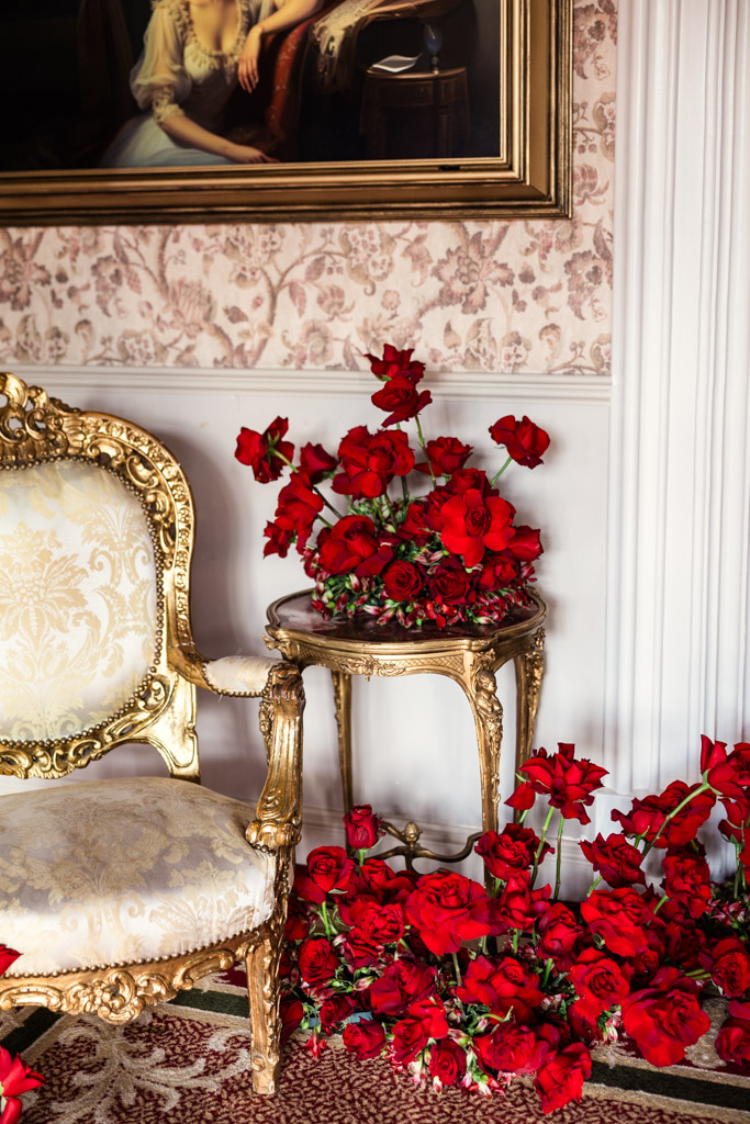 A gold ornate chair beside a table with vibrant red roses and more roses scattered on the floor inside Markree Castle