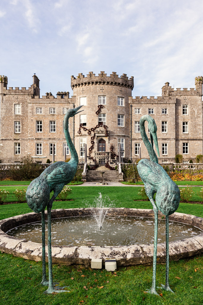 Two flamingo statues by a fountain in front of Markree Castle with turrets and manicured gardens