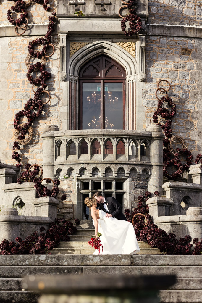 Bride and groom kiss in front of Markree Castle, its steps adorned with red floral arrangements