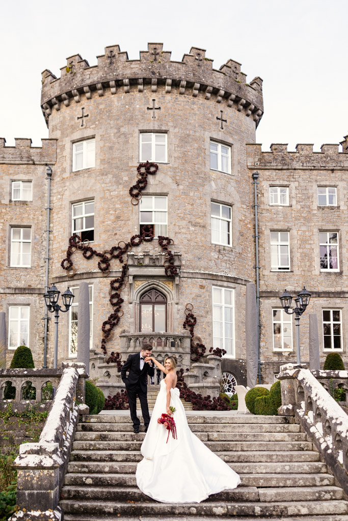 Groom kisses bride's hand as they stand on stone steps in front of Markree Castle