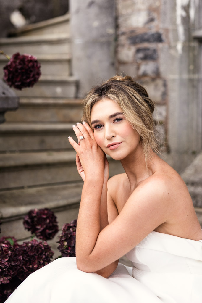 Portrait of bride in a white dress posing by stone steps at Markree Castle, showing off an wedding ring on her left hand