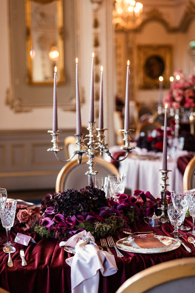 Guest table setting with tall candles, dark flowers, crystal glasses, and a rich burgundy tablecloth for Markree Castle wedding reception