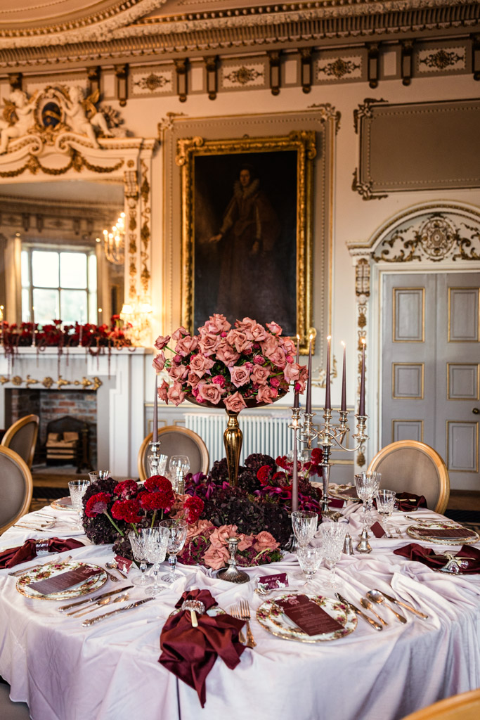 Guest table with red and pink flowers, elegant tableware, and ornate decor in a grand room for a Markree Castle wedding reception