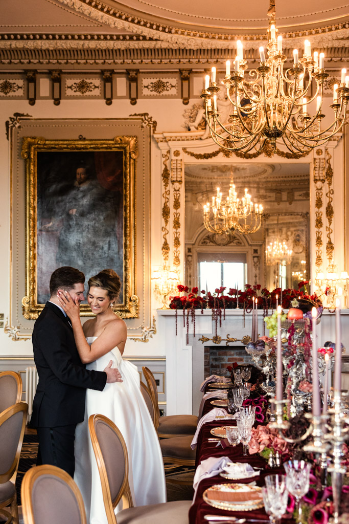 A bride and groom embrace in an ornate, chandelier-lit room set for their wedding reception at Markree Castle