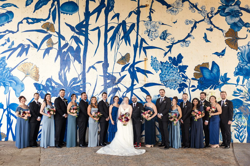 Wedding party portrait in front of a blue and white floral mural at Ping Tom Memorial Park