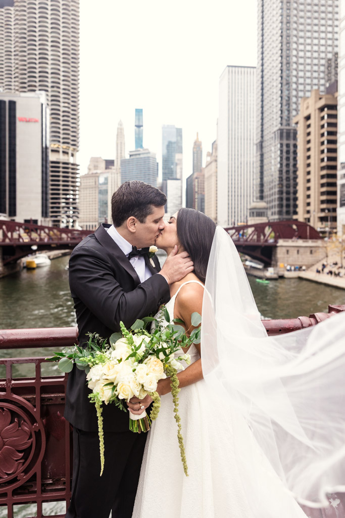 Bride and groom kiss on the LaSalle Street Bridge in downtown Chicago, skyscrapers and river behind them