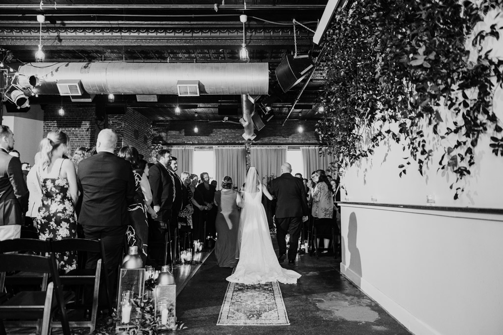 Black and white photo of bride walking down the aisle at a Bottom Lounge wedding, guests standing on either side