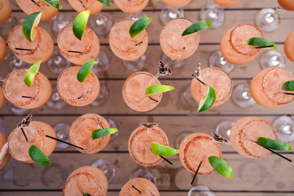 Overhead view of several pink cocktails with lime wedges and salt rims arranged on a wooden surface for Bottom Lounge wedding celebration
