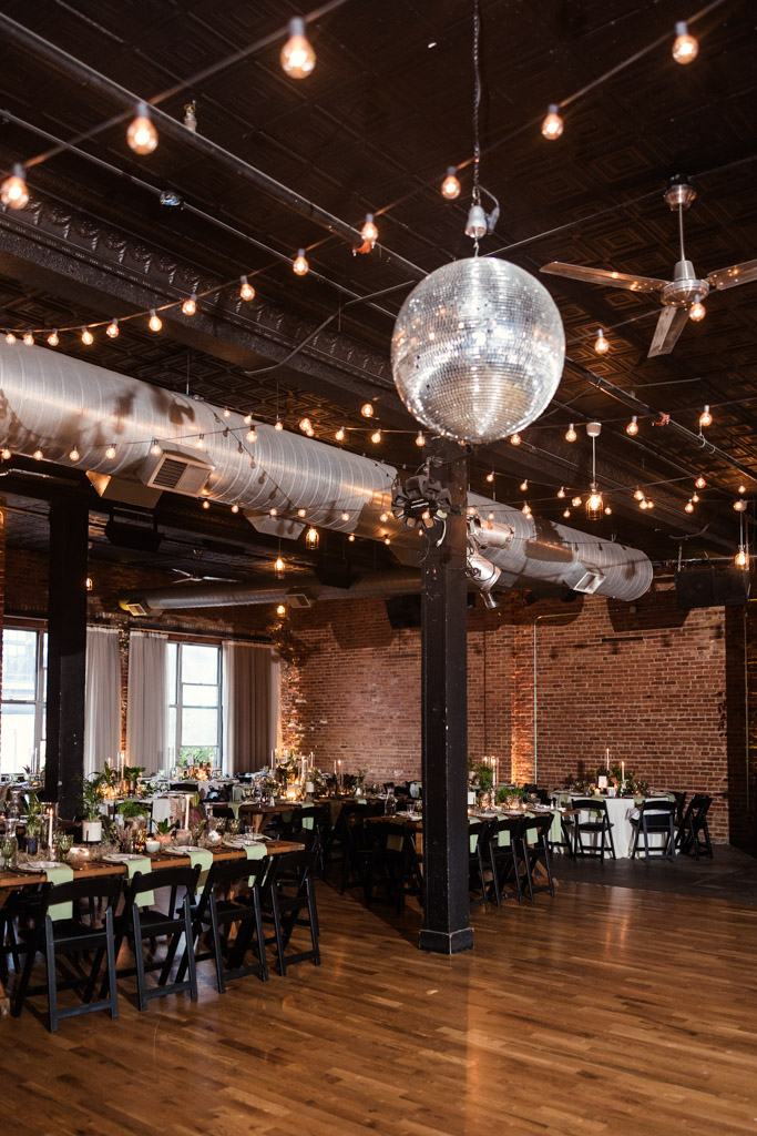 Wedding reception space at Bottom Lounge with brick walls, string lights, a large disco ball, and decorated dining tables