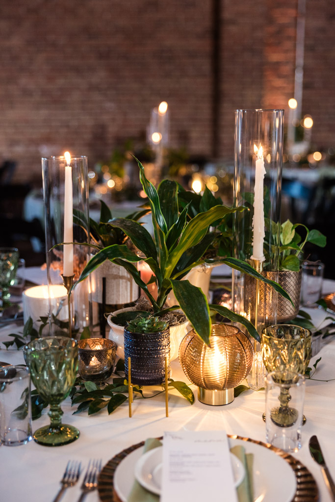 Guest table setting at a Bottom Lounge wedding reception, featuring green plants, candles in glass holders, and green glassware on a crisp white tablecloth