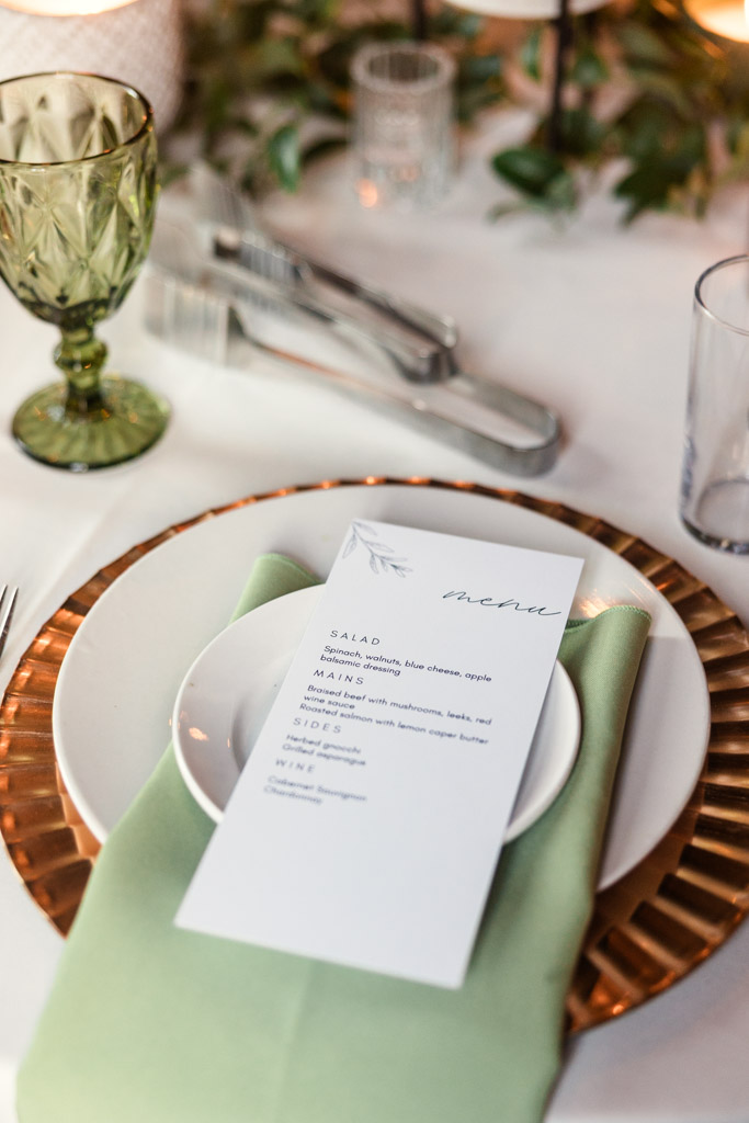 Guest table setting for Bottom Lounge wedding reception featuring a green napkin, gold charger, and a printed menu on a white plate