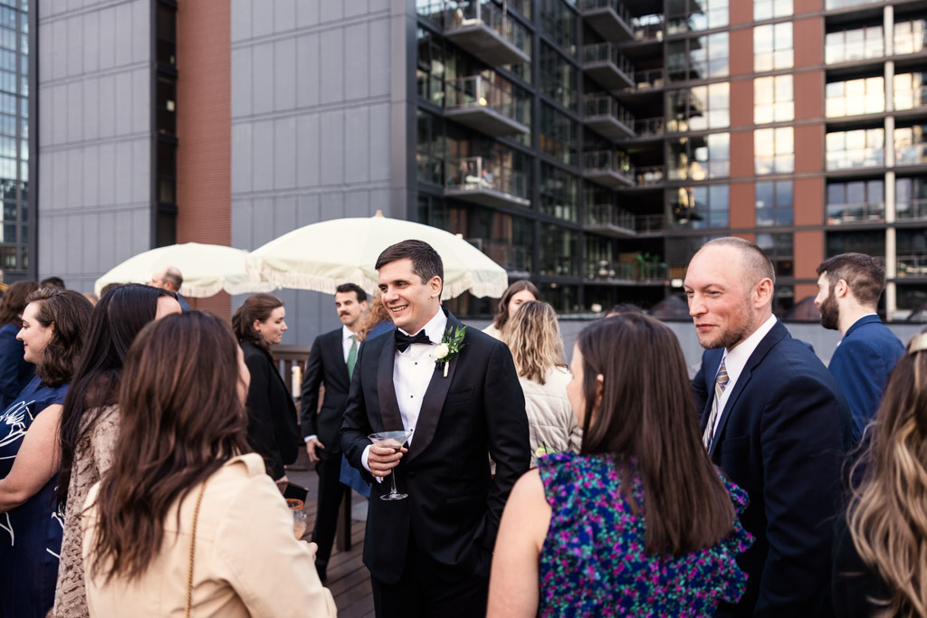 Groom speaks with guests during cocktail hour on the rooftop deck of Bottom Lounge