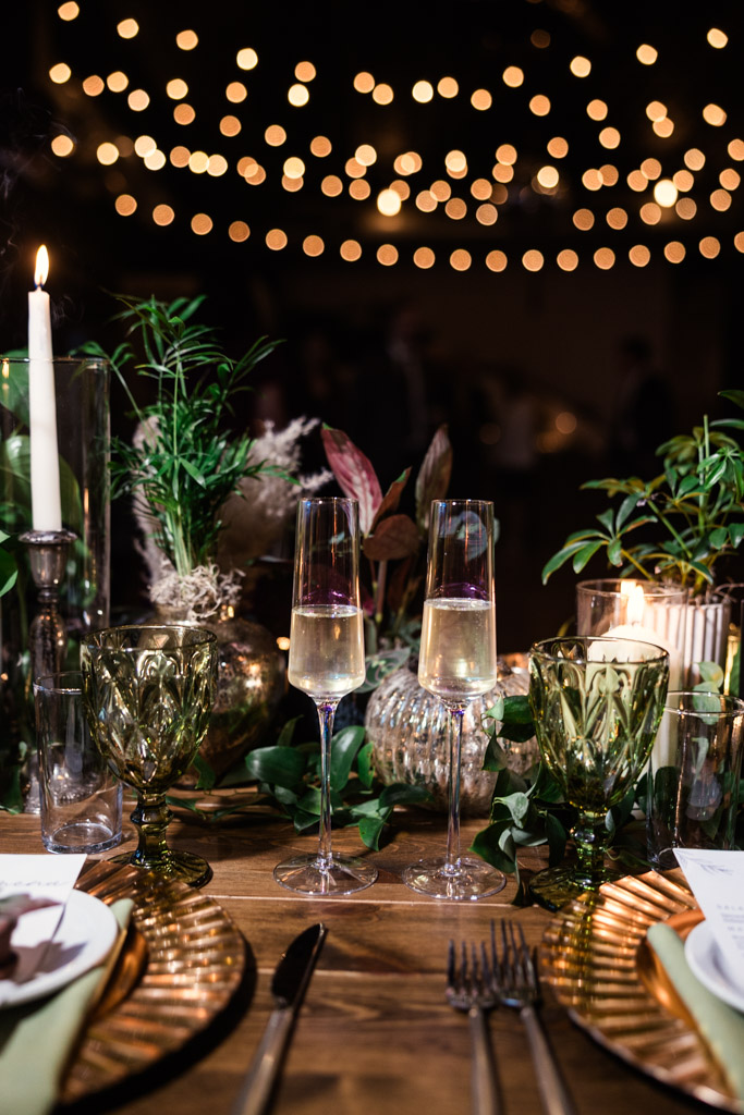 Two glasses of champagne on a decorated table with candles, greenery, and string lights for Bottom Lounge wedding reception