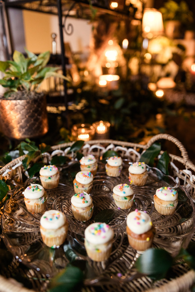 Mini cupcakes with white frosting and sprinkles on a tray, surrounded by plants and warm lights for a Bottom Lounge wedding celebration