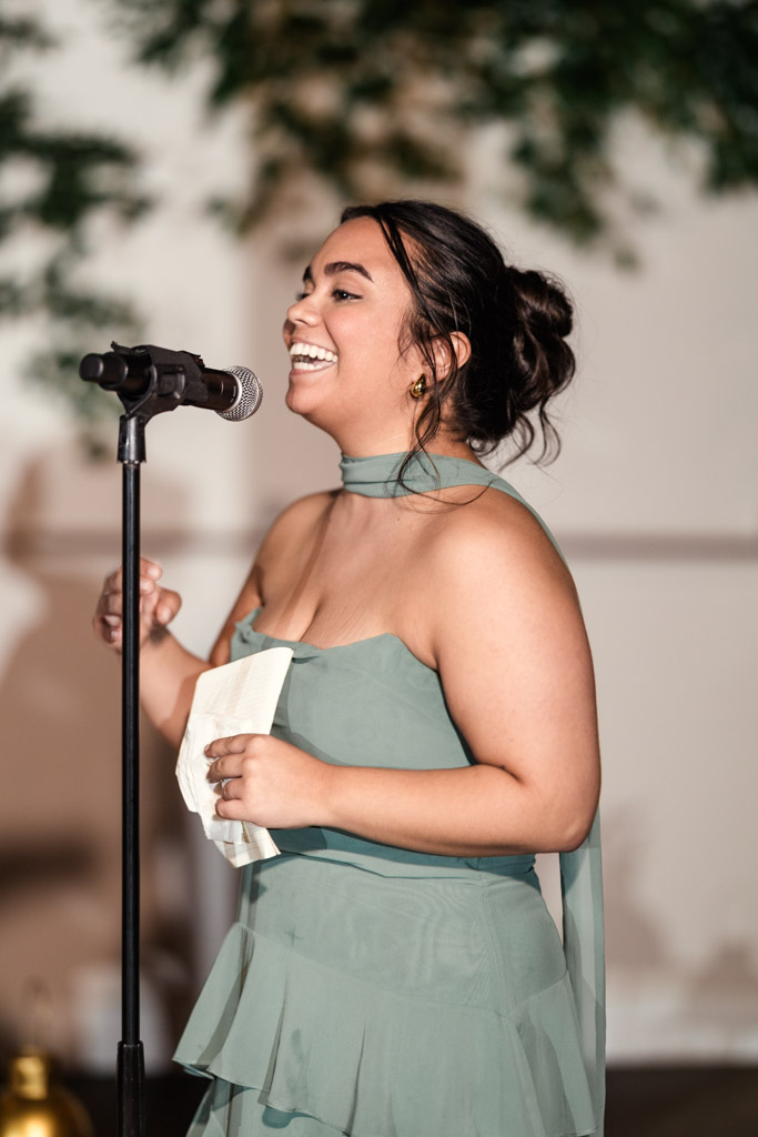 Maid of Honor in a green dress smiling and speaking into a microphone at a Bottom Lounge wedding reception