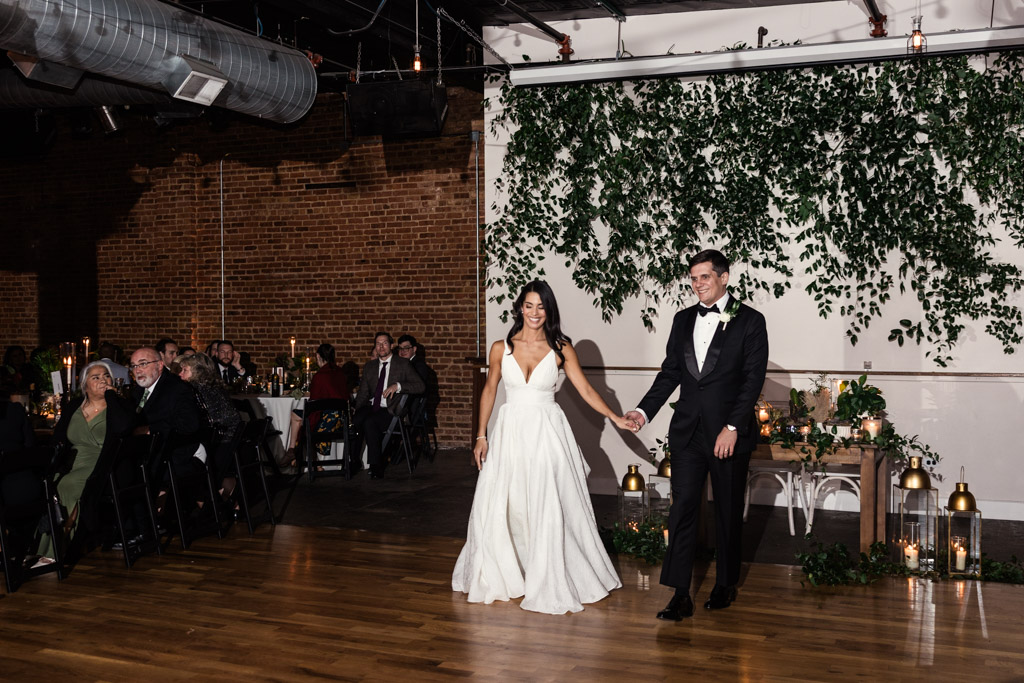 A bride and groom hold hands before their first dance during their Bottom Lounge wedding reception, smiling at guests
