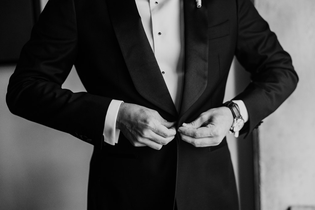 Black and white photo of groom buttoning his tuxedo jacket before his Bottom Lounge wedding
