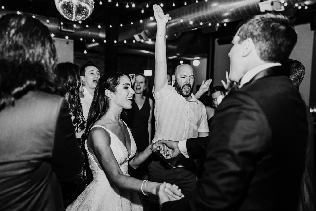 Black and white photo of bride and groom dancing joyfully with guests at their Bottom Lounge wedding reception
