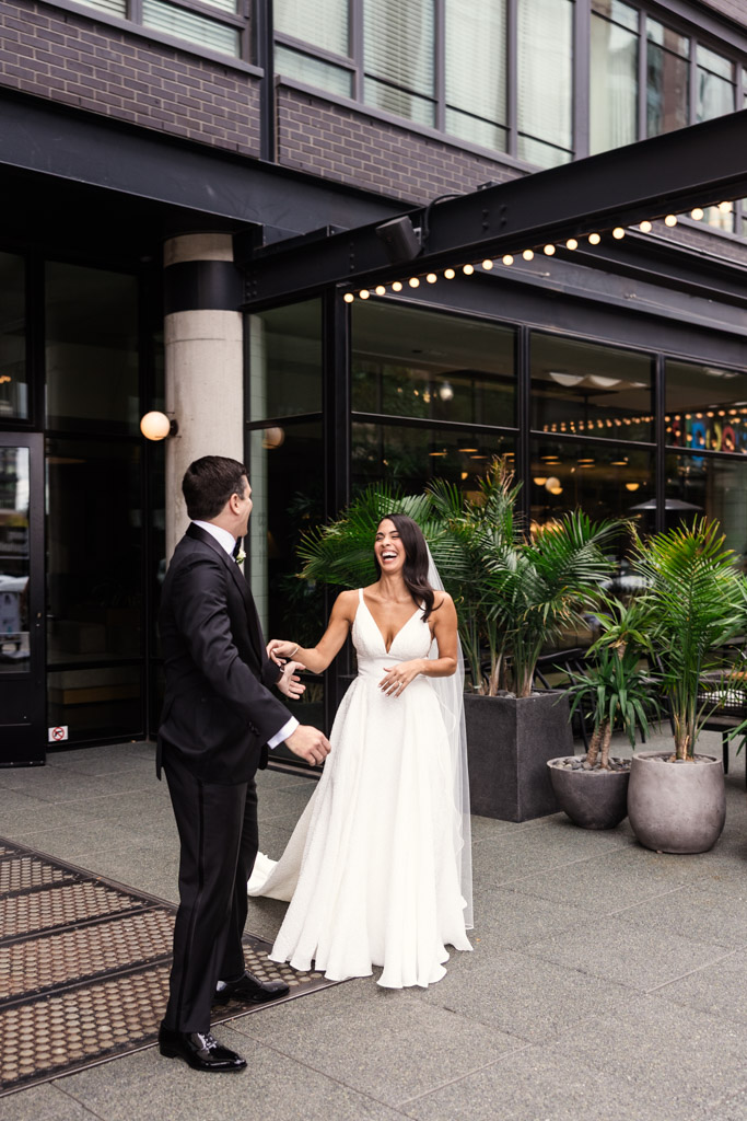 A bride and groom smile and laugh outside The Emily Hotel during their first look