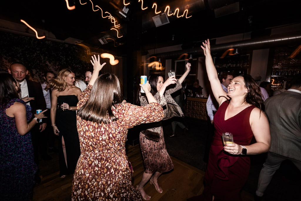 Guests dancing and celebrating at a Bottom Lounge wedding reception, hands raised, drinks in hand