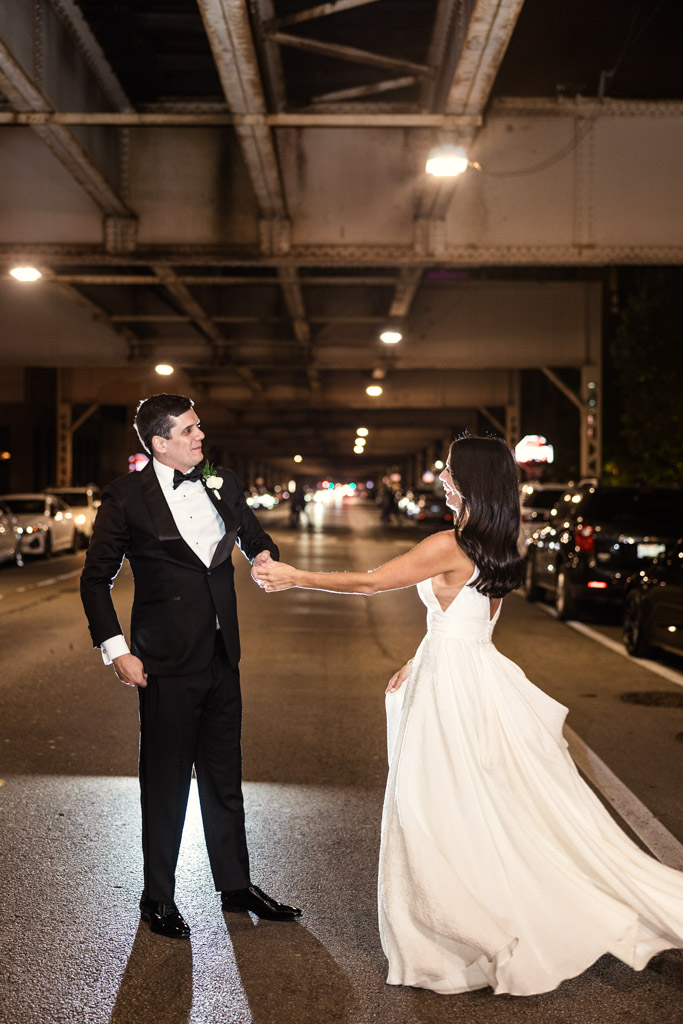 Bride and groom in formal attire dance together under a n elevated train track at night during their Bottom Lounge wedding reception