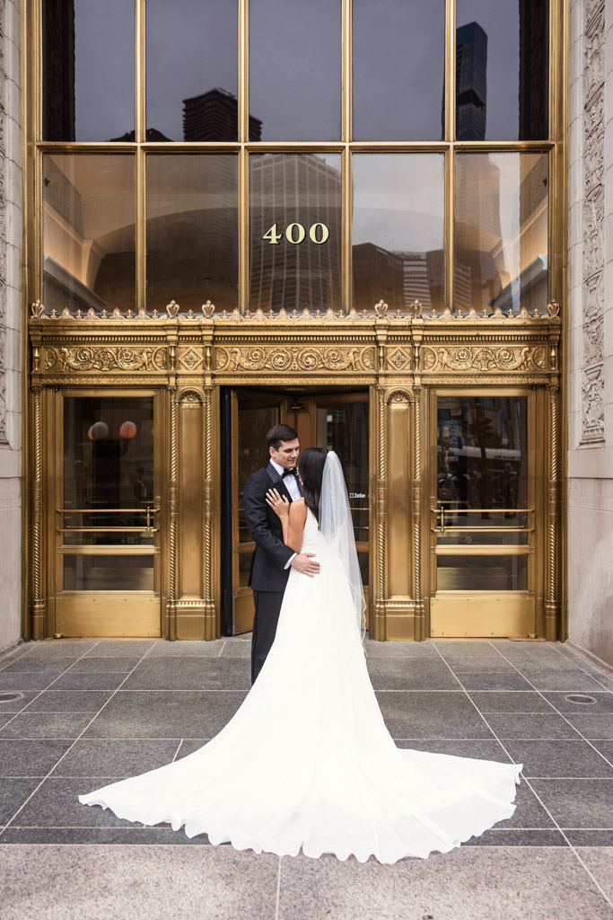 A bride and groom hold each other in front of Wrigley Building entrance before their Bottom Lounge wedding