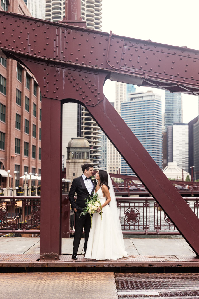 A bride and groom stand on the LaSalle Street Bridge, gazing at each other with skyscrapers in the background