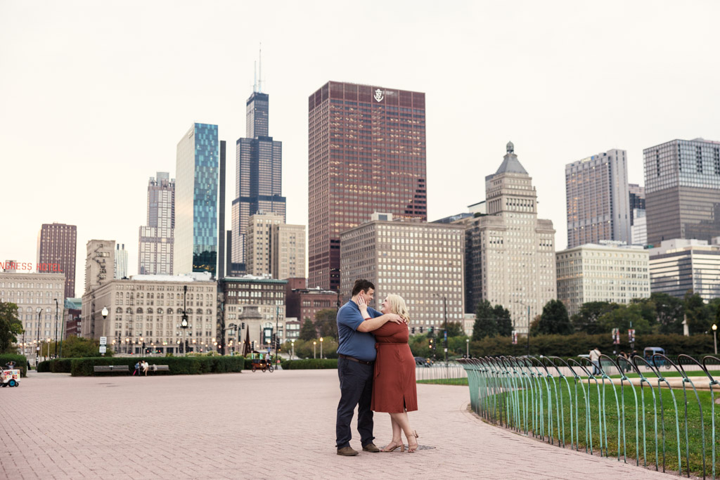 A couple embraces near Buckingham Fountain with Chicago skyscrapers providing a backdrop during their South Loop engagement session