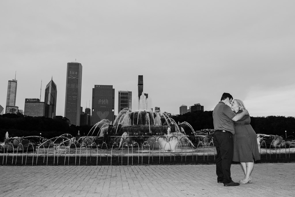 Black and white photo of couple in front of Buckingham Fountain with the Chicago skyline in the background during their South Loop engagement session