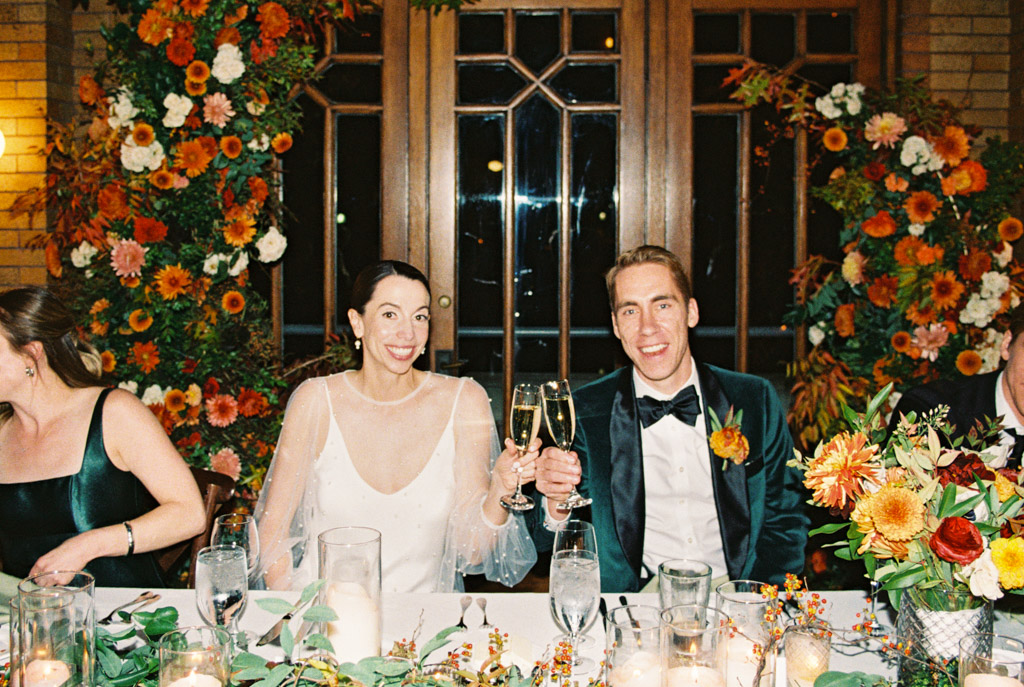 Film photo of bride and groom in formal attire smiling and toasting at their Cafe Brauer wedding reception