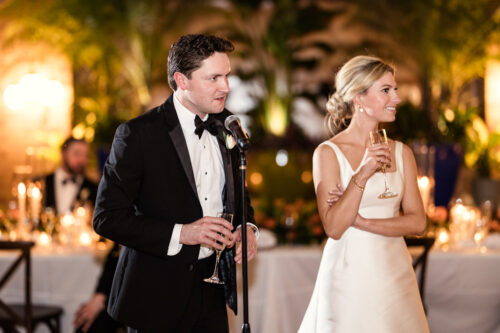 A man in a tuxedo and a woman in a white dress give a toast with champagne at a formal event, celebrating the Best of 2025.
