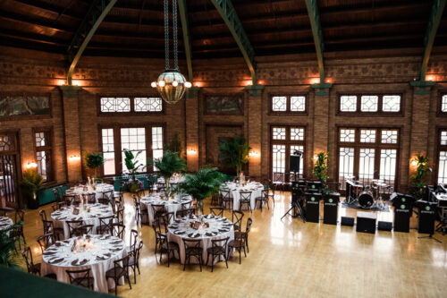 Large, elegant banquet hall with round tables set for a Best of 2025 event, featuring wooden floors and musical equipment on stage.