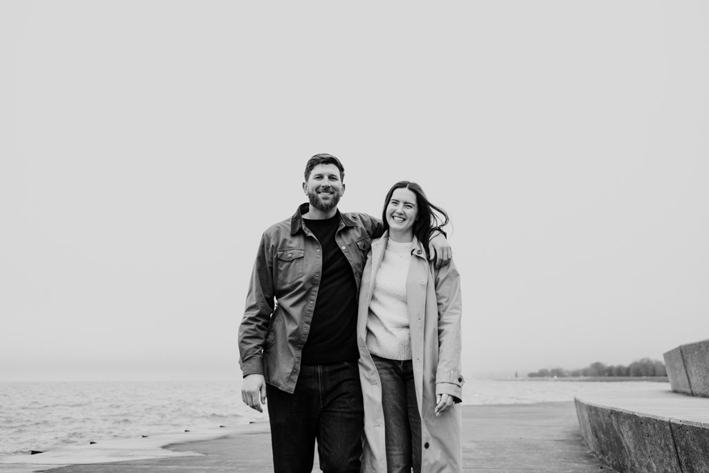 Black and white portrait of happy couple arm in arm by Lake Michigan at Belmont Harbor on a cloudy day