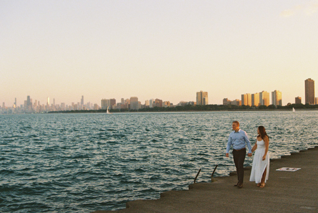Film photo of engaged couple walking along Lake Michigan with Chicago skyline in the background at sunset