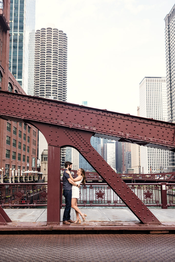 A couple embraces on LaSalle Street bridge during their Chicago summer engagement, with tall city buildings rising in the background