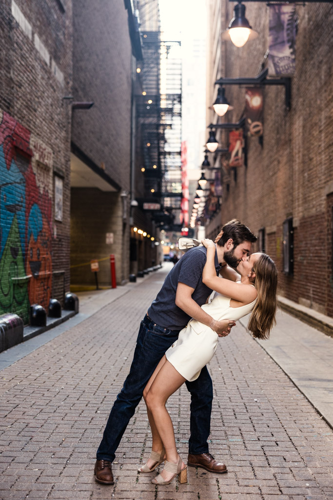 A couple kisses passionately in an urban alley, surrounded by brick walls and street art during a vibrant Chicago summer engagement.