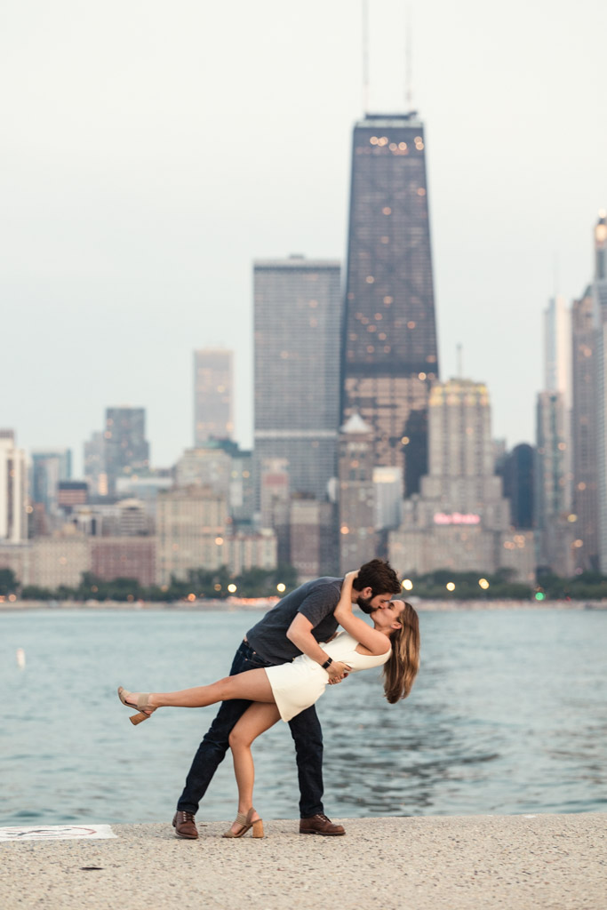 A couple dances and dips on a waterfront at North Avenue Beach with the Chicago skyline in the background during their Chicago summer engagement session