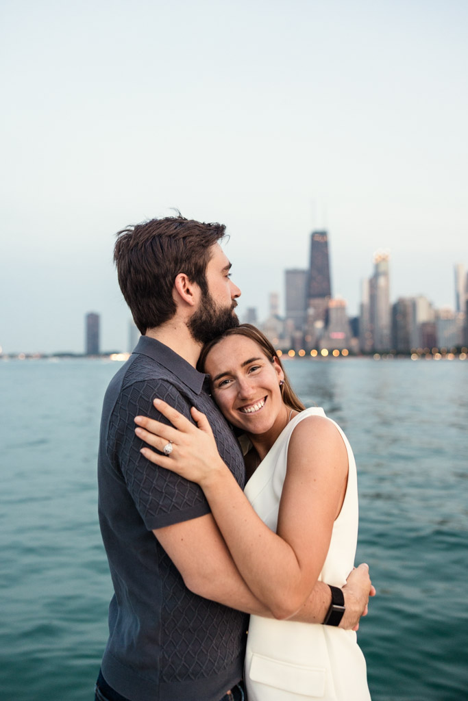 A couple embraces by Lake Michigan during their Chicago summer engagement session with the city skyline behind them